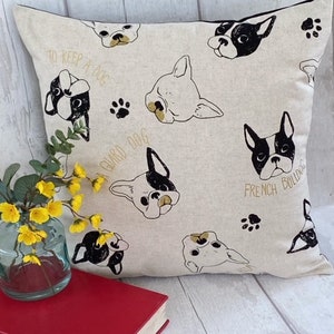 May include: A beige throw pillow with a black and white French Bulldog pattern. The pillow has the text "To keep a dog, a guard dog, French Bulldog" printed on it.