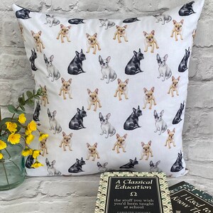 May include: White cushion cover with a repeating pattern of black, white and tan French bulldog illustrations. The cushion is sitting on a white brick surface next to two books. The top book has the title "A Classical Education" and the bottom book has the title "I Used to Know That".