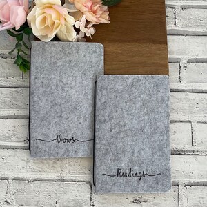 May include: Two grey felt notebooks with black stitching and the words "Vows" and "Readings" written in black cursive on the front.