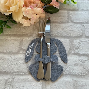 May include: Grey felt bunny-shaped place card holder with a fork and knife inside. The name "Charlie" is written on the holder.
