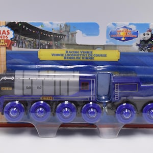 May include: A blue and silver Thomas & Friends Wooden Railway train engine named Racing Vinnie. The engine has a black face with a silver stripe and the name "Vinnie" printed on it. The engine has six wheels and is made of wood.