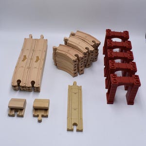 May include: A set of wooden train track pieces, including curved tracks, straight tracks, and a bridge. The tracks are made of natural wood and are in good condition. The bridge is red and has a tunnel opening.