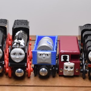 May include: A collection of wooden toy trains in various colors, including red, black, and blue. Each train features a smiling face and is designed with different details, such as a cargo car and a dragon-shaped carriage.