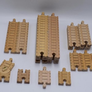 May include: A set of wooden train track pieces, including straight tracks, curved tracks, and a points track. The tracks are made of natural wood and have a light brown colour.