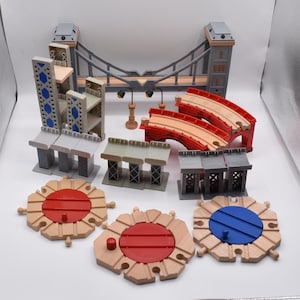 May include: A toy train set featuring a gray suspension bridge, two red arched track sections, three gray bridge supports, two street lamps, and three circular wooden track pieces with red and blue centers, including one red and one blue knob.