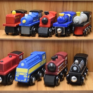 Pode incluir: Uma coleção de comboios de brinquedo de madeira coloridos exibidos em prateleiras de madeira. Os comboios são pintados em várias cores, incluindo vermelho, azul e preto, com detalhes prateados. Cada comboio tem um design único.