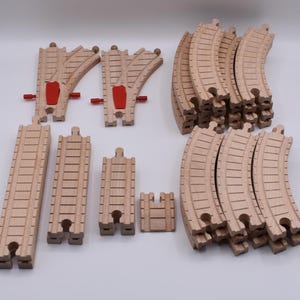 May include: A selection of wooden toy train tracks and points. The set includes curved and straight track pieces, along with red and wooden points. The tracks are made of light-coloured wood.