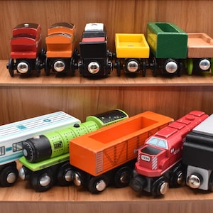 May include: Wooden toy train set with various colored train cars. The set includes red, orange, black, yellow, green, and white cars. The train cars are displayed on wooden shelves.