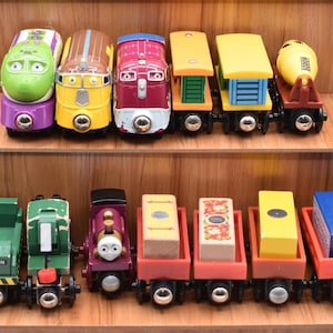 May include: A selection of brightly coloured toy trains arranged on wooden shelves. The trains are in various colours, including green, yellow, red, and purple. Some have cargo, while others are engines.