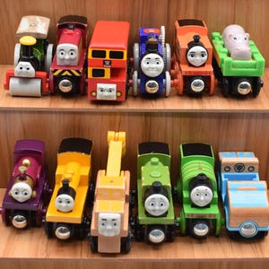 Può includere: Una collezione di trenini giocattolo in legno colorati, tra cui locomotive e vagoni. I treni presentano vari colori come rosso, verde, blu e giallo, con facce sorridenti. Alcuni vagoni trasportano animali.