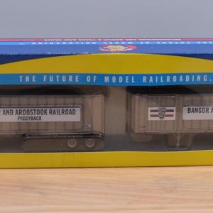 May include: A blue and yellow cardboard box containing two model Bangor and Aroostook Railroad piggyback trailers. The box features the text "The Future of Model Railroading" and a green starburst graphic with the text "New Tooling!" on the front.