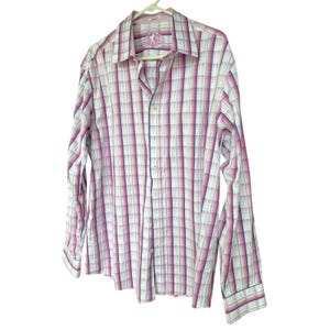 May include: A long-sleeved button-down shirt with a plaid pattern in white, pink, and purple. The shirt is hanging on a white hanger. The collar and cuffs have a contrasting trim. The shirt has a small emblem on the chest.