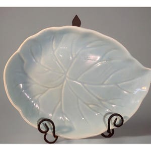 May include: A light blue ceramic leaf-shaped serving dish with a raised leaf design. The dish is on a black metal stand.