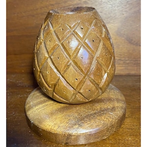 May include: A wooden pineapple shaped bowl with a carved design and holes. The bowl is sitting on a wooden base.