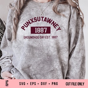 Puede incluir: Una sudadera gris con un gráfico marrón que dice "PUNXSUTAWNEY 1887 GROUNDHOG DAY EST. 1887".
