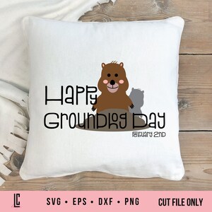 May include: A white pillow with the text "Happy Groundhog Day" and the date "February 2nd" in black. A brown groundhog with pink cheeks is peeking out of a hole in the ground.