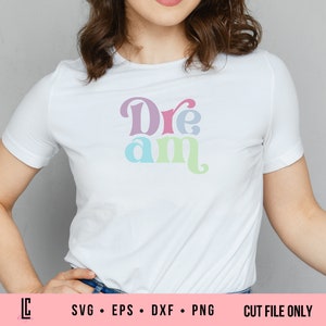 Puede incluir: Una camiseta blanca con la palabra "Dream" escrita en letras estilizadas de colores. Las letras son en tonos de rosa, azul, verde y morado.