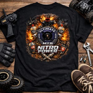 May include: Black t-shirt featuring a detailed graphic with the words "ULTIMATE NITRO POWER" and "MTS". The design includes images of model car engines, fuel bottles, and flames. Additional items include a remote control, gloves, and a pair of shoes.