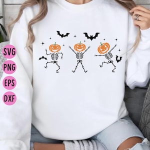 May include: A white long-sleeve sweatshirt featuring a graphic print of three skeletons with orange pumpkin heads in various dancing poses, surrounded by black silhouettes of flying bats and small four-pointed stars, with SVG, PNG, EPS, DXF text.