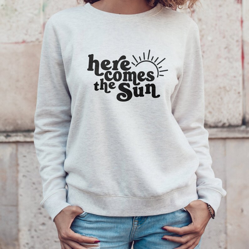 May include: White sweatshirt with a black graphic print that says "here comes the sun" with a stylized sun graphic.