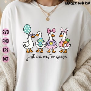 Puede incluir: Camiseta blanca con una ilustración de dibujos animados de cuatro gansos celebrando la Pascua. Los gansos están decorados con huevos de Pascua, una zanahoria y un globo de lunares. El texto "just an easter goose" está escrito debajo.
