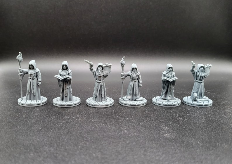 May include: Set of six gray painted miniature figures of robed figures holding various objects, including a book, a staff, and a sword. The figures are standing on round bases.