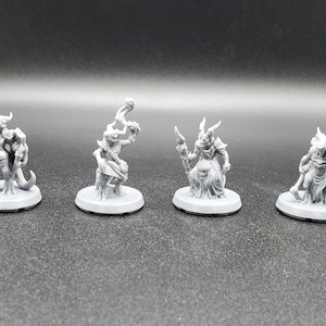 May include: Four gray painted miniature figurines of fantasy creatures with horns and holding various weapons and staffs. The figures are standing on round bases.
