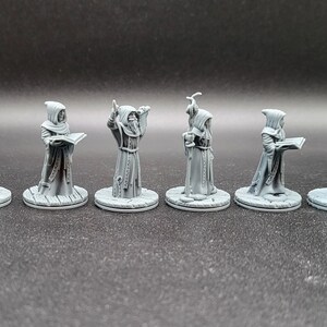 May include: Six gray painted miniature figurines of robed figures, each with a different pose and holding a different object. The figures are standing on round bases.