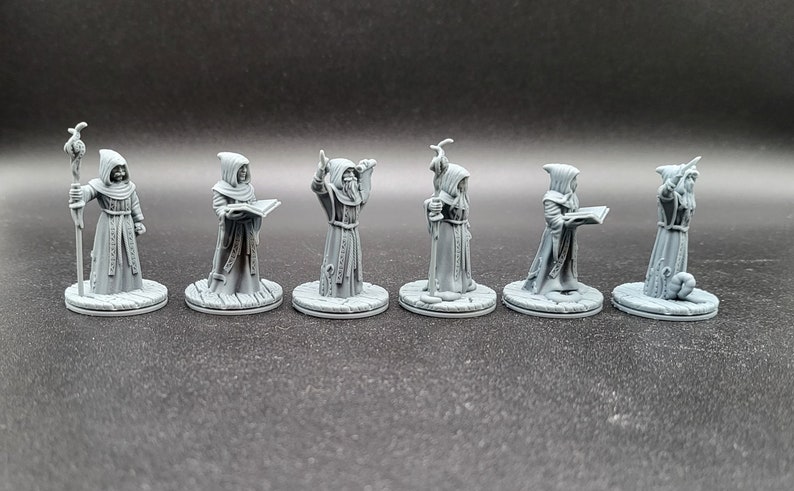 May include: Six gray painted miniature figurines of robed figures, each with a different pose and holding a different object. The figures are standing on round bases.