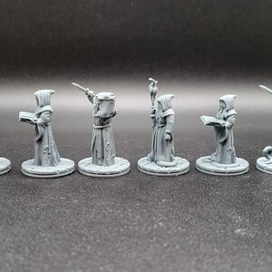 May include: Seven gray plastic miniature figures of robed figures with different poses and accessories, including a staff, a book, and a sword. The figures are standing on round bases.