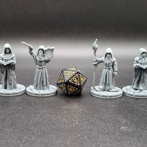 May include: Seven gray painted miniature figures of robed figures holding various objects, including a book, a staff, and a dagger. A black and gold dice is in the center of the image.