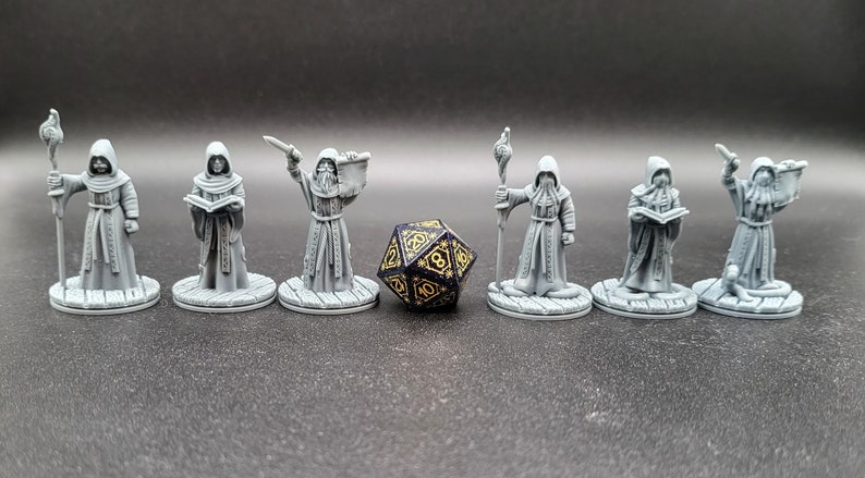 May include: Seven gray painted miniature figures of robed figures holding various objects, including a book, a staff, and a dagger. A black and gold dice is in the center of the image.