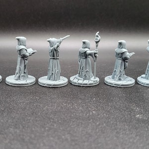 May include: Seven gray painted miniature figures of robed wizards, each holding a different magical item, standing on round bases.