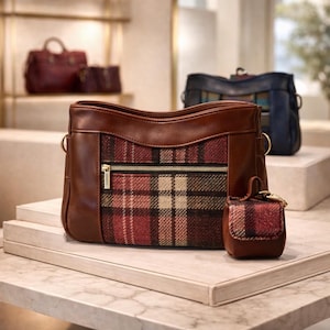 May include: A brown leather handbag with a plaid fabric center panel and a gold zipper. A smaller matching coin purse sits next to the handbag. Other handbags are visible in the background.