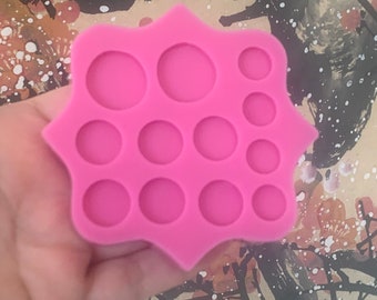 Könnte beinhalten: Rosa Silikonform mit 13 runden Kreisen in verschiedenen Größen. Die Form ist sternförmig mit abgerundeten Kanten.