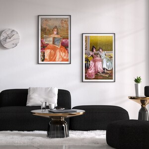 May include: Two framed paintings of women in vintage dresses reading books. The paintings are hanging on a white wall above a black couch and a coffee table.