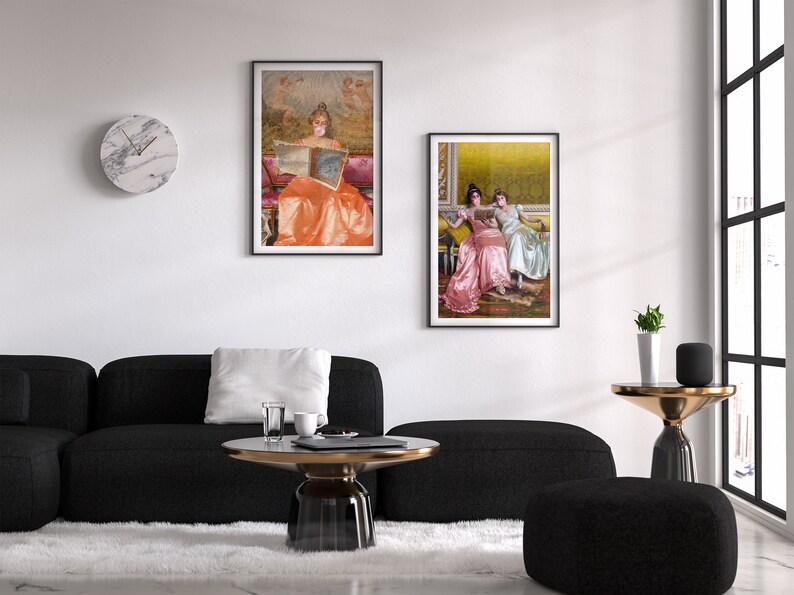 May include: Two framed paintings of women in vintage dresses reading books. The paintings are hanging on a white wall above a black couch and a coffee table.