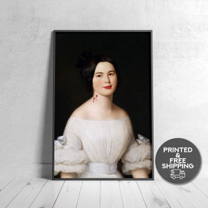 May include: A framed portrait of a woman in a white off-the-shoulder dress with puffed sleeves. The woman has dark hair and red lipstick. There are two small red marks on her neck. The frame is black. A circular graphic with text is in the lower right corner.