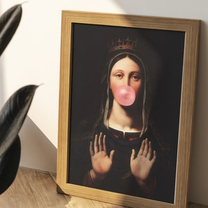 Pu&ograve; includere: Una stampa incorniciata di una donna che indossa una corona e una veste blu, con un grande chewing gum rosa in bocca. Lo sfondo &egrave; scuro.