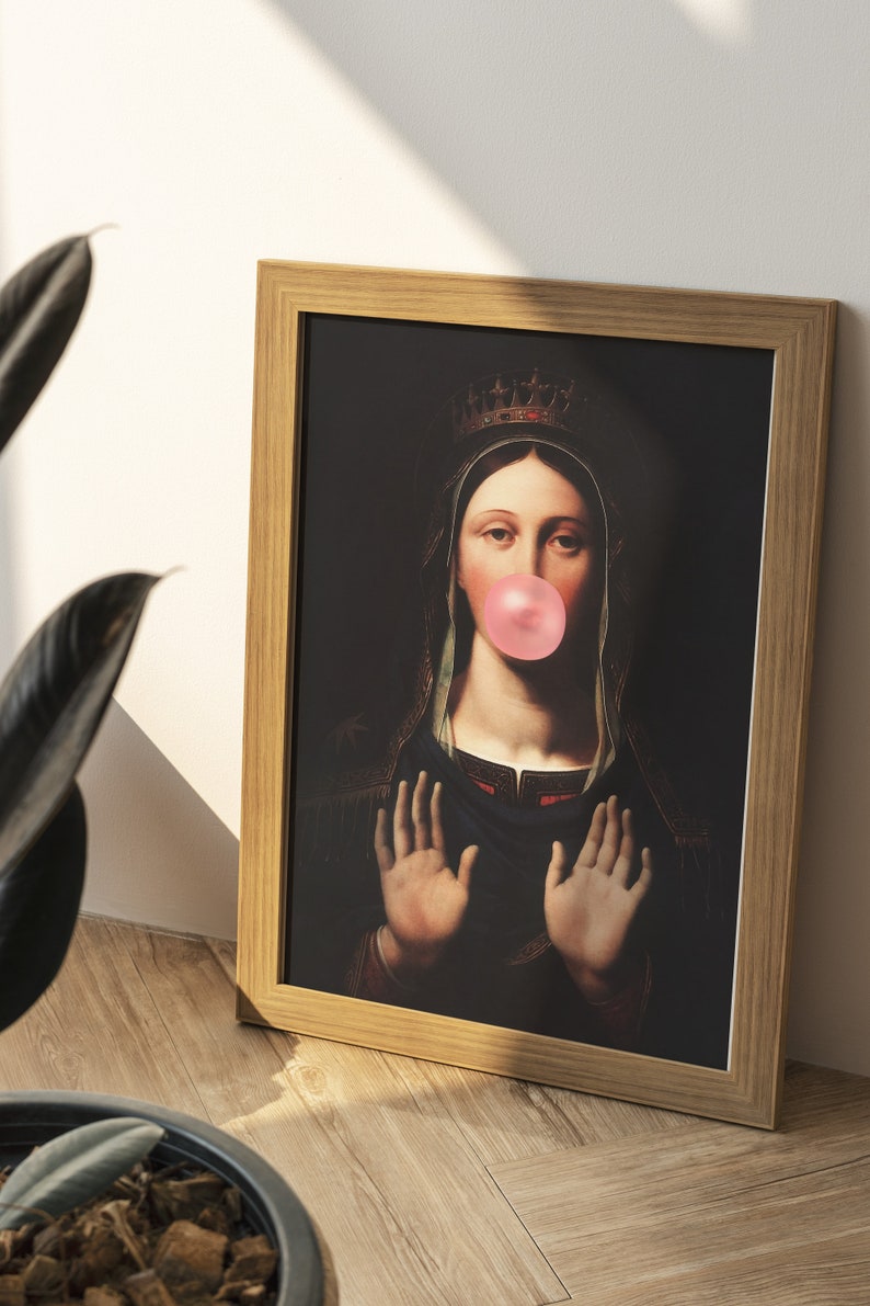 Pu&ograve; includere: Una stampa incorniciata di una donna che indossa una corona e una veste blu, con un grande chewing gum rosa in bocca. Lo sfondo &egrave; scuro.