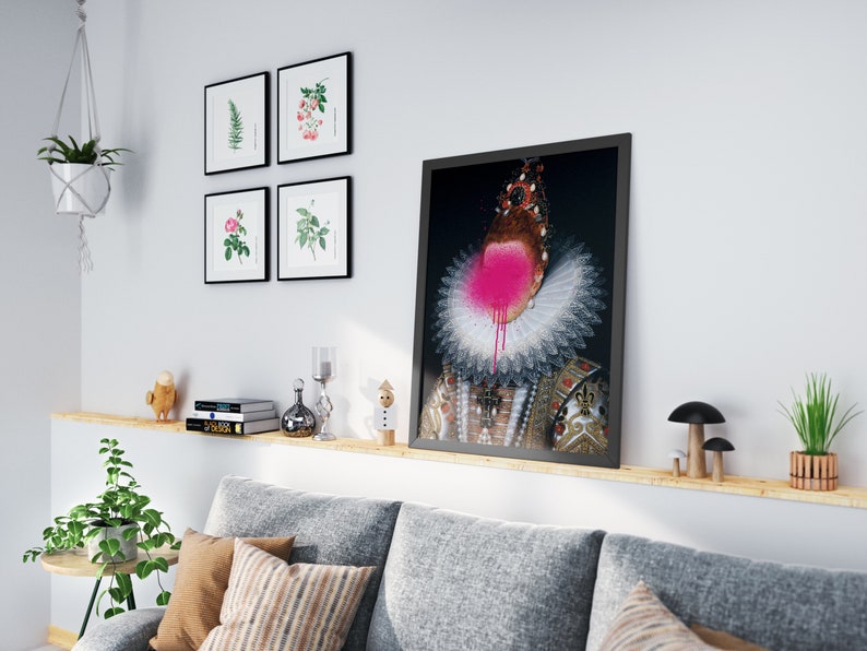 May include: A framed print of a portrait of a person wearing a white ruff collar and a gold and black patterned dress. The person's face is covered in pink spray paint.