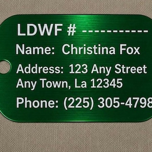 May include: A green metal tag with white text. The tag includes the text "LDWF #", a name, address, and phone number. The tag has a hole on the left side.