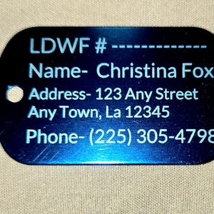 May include: A blue metal dog tag with the text "LDWF #", "Name- Christina Fox", "Address- 123 Any Street, Any Town, La 12345", and "Phone- (225) 305-4798". The tag has a hole at the top.