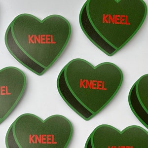 May include: Eight green heart-shaped stickers with the word "Kneel" printed in red letters on each sticker.