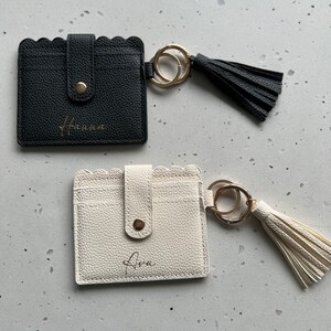 May include: Two cardholders with scalloped edges and keychains. One is black with "Hanna" in gold script, the other is off-white with "Ava" in gold script. Each has a gold button closure and a matching tassel.