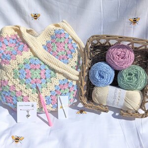 Puede incluir: Una bolsa de mano de crochet de forma granny square con hilo rosa pastel, azul y verde. La bolsa viene con cuatro ovillos de hilo de los mismos colores, un ganchillo y un marcador de punto.