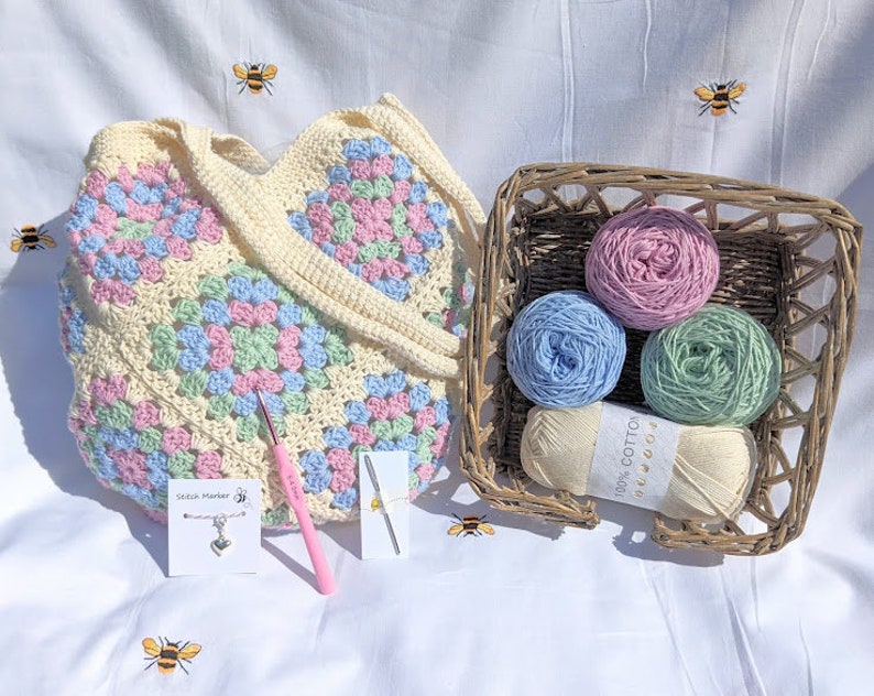 Puede incluir: Una bolsa de mano de crochet de forma granny square con hilo rosa pastel, azul y verde. La bolsa viene con cuatro ovillos de hilo de los mismos colores, un ganchillo y un marcador de punto.