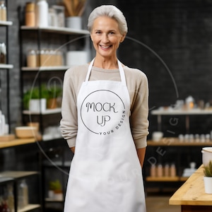 May include: A white apron with a black circle that says "Mock Up Your Design" on it. A woman is wearing the apron and smiling at the camera.