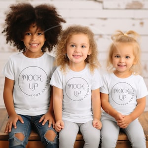 May include: Three children wearing white t-shirts with a black circle and the text "Mock Up Your Design" printed on them. The children are sitting on a wooden bench.