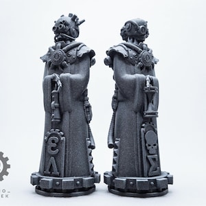 Könnte beinhalten: Zwei graue Statuen von bekleideten Figuren mit mechanischen Masken und komplizierten Details. Jede Figur hält eine Laterne und weist ein Zahnraddesign auf. Der Sockel jeder Statue hat ein geometrisches Muster. Der Text "TECHNO_HERETEK" ist sichtbar.